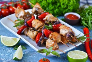 Barbecue of chicken on skewers with vegetables on a blue concrete background. Picnic.